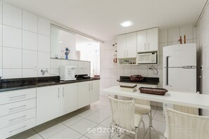 Une cuisine moderne avec des meubles blancs, un four à micro-ondes, un réfrigérateur et un coin repas doté de chaises en osier.
