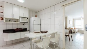 A modern kitchen with white cabinetry, a white countertop, and a dining area with white chairs.