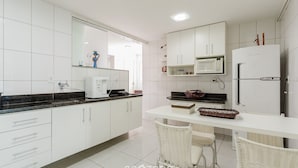 A modern kitchen with white cabinets, a microwave, a refrigerator, and a dining area with wicker chairs.