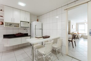 Une cuisine moderne avec des meubles blancs, un plan de travail blanc et un coin repas avec des chaises blanches.