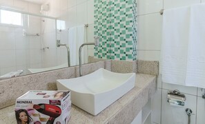 Une salle de bain avec un lavabo sur colonne blanc, un miroir, une douche et un mur recouvert de carreaux.