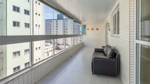 A balcony with a view of high-rise buildings, a tiled floor, and a dark-colored sofa with cushions.