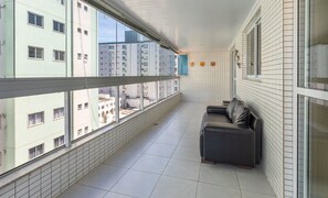 A balcony with a view of high-rise buildings, a tiled floor, and a dark-colored sofa with cushions.