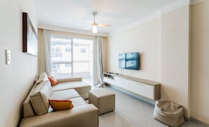 Un salon moderne avec un ensemble de canapés, un téléviseur fixé au mur et un ventilateur de plafond.