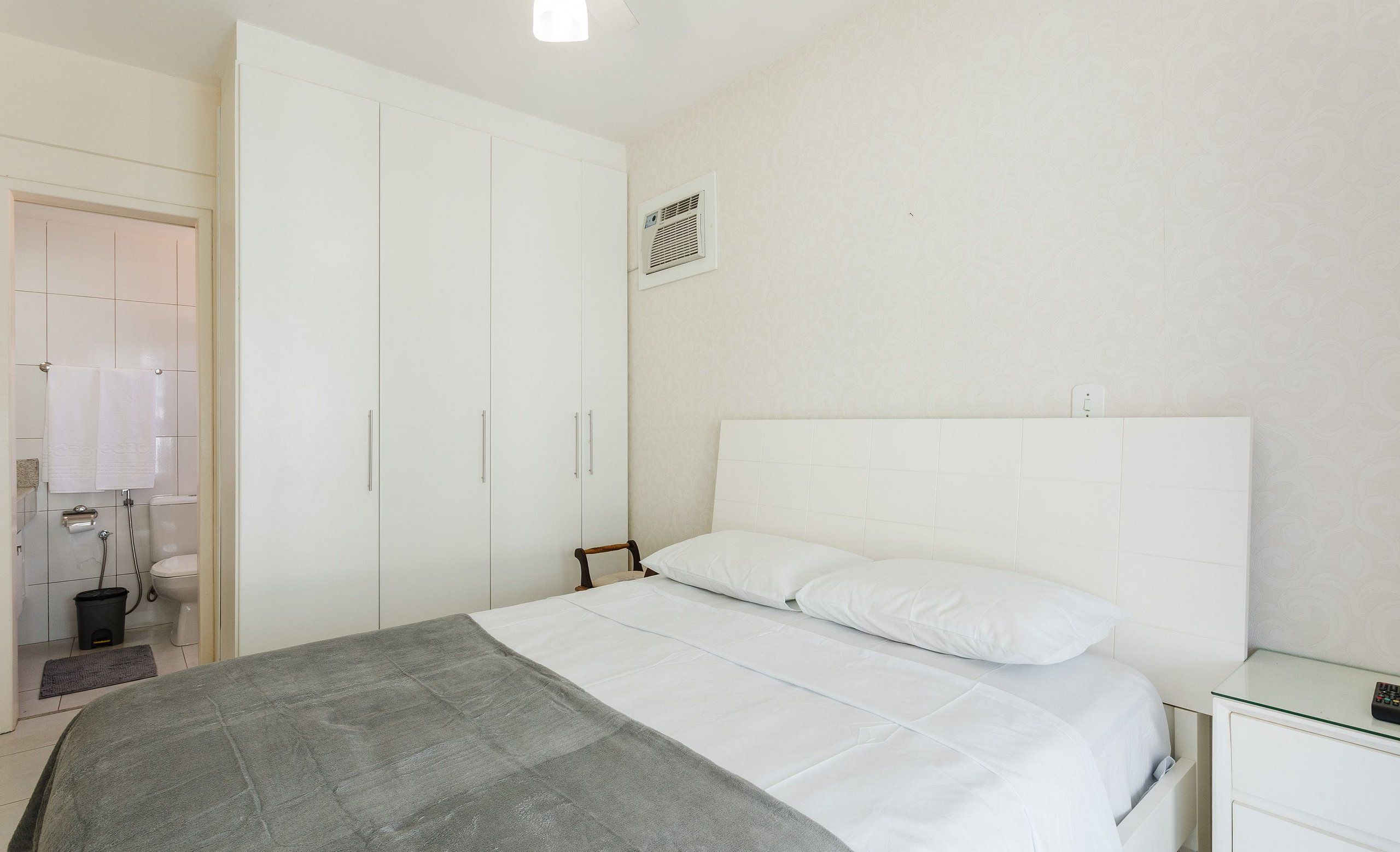 A bedroom with a bed, a wardrobe, a bedside table, and a small desk.