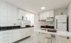 A modern kitchen with white cabinets, a microwave, a refrigerator, and a dining area with wicker chairs.