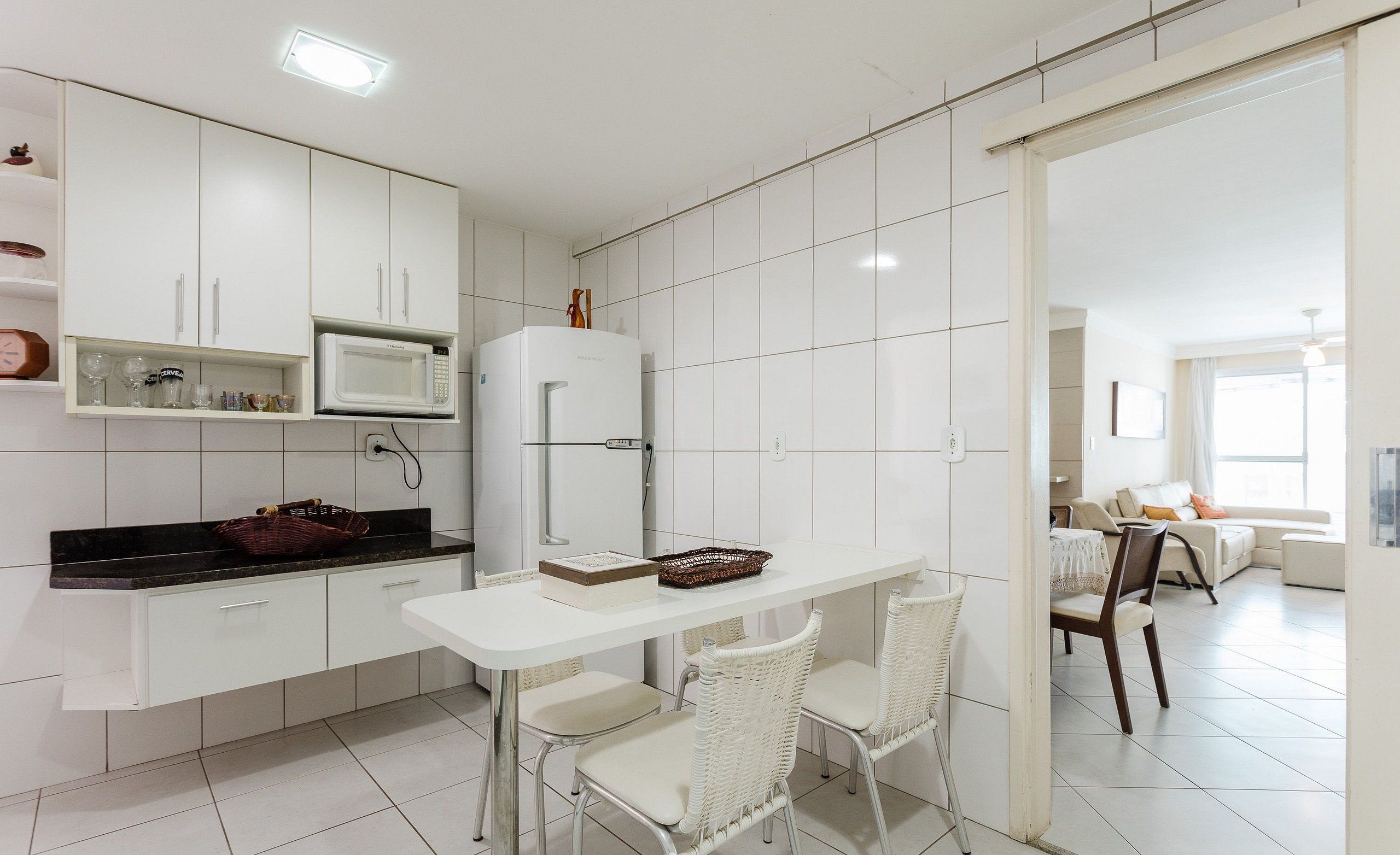 Una cocina moderna con armarios blancos, una encimera blanca y una zona de comedor con sillas blancas.