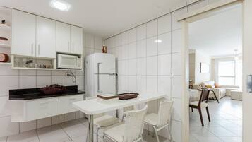 Una cocina moderna con armarios blancos, una encimera blanca y una zona de comedor con sillas blancas.