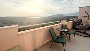 A balcony with a view of a forested landscape and mountains, featuring a table, two chairs, and a hanging chair.
