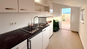 A modern kitchen with a black countertop, stainless steel sink, and white cabinets. There is a green chair outside the door.