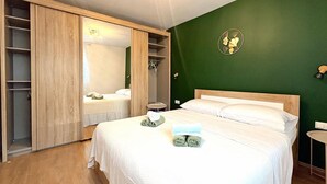 A bedroom with a bed, a wooden wardrobe, a green accent wall, and a mirror.