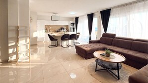 A modern living room with a brown sofa, a round coffee table, and a dining area with chairs and a kitchen in the background.