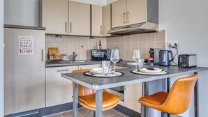 A modern kitchen with a dining table, two chairs, a stove, a microwave, and a kettle. - Célestine, mignon F2 en centre ville de Rouen - Proximité Donjon de Rouen (Rouen)