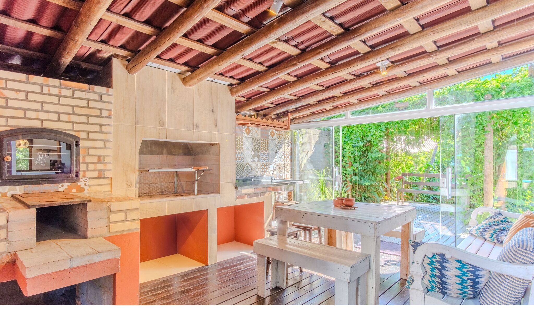 A patio with a brick oven, outdoor seating, and a view of greenery.