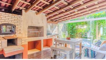 A patio with a brick oven, outdoor seating, and a view of greenery.
