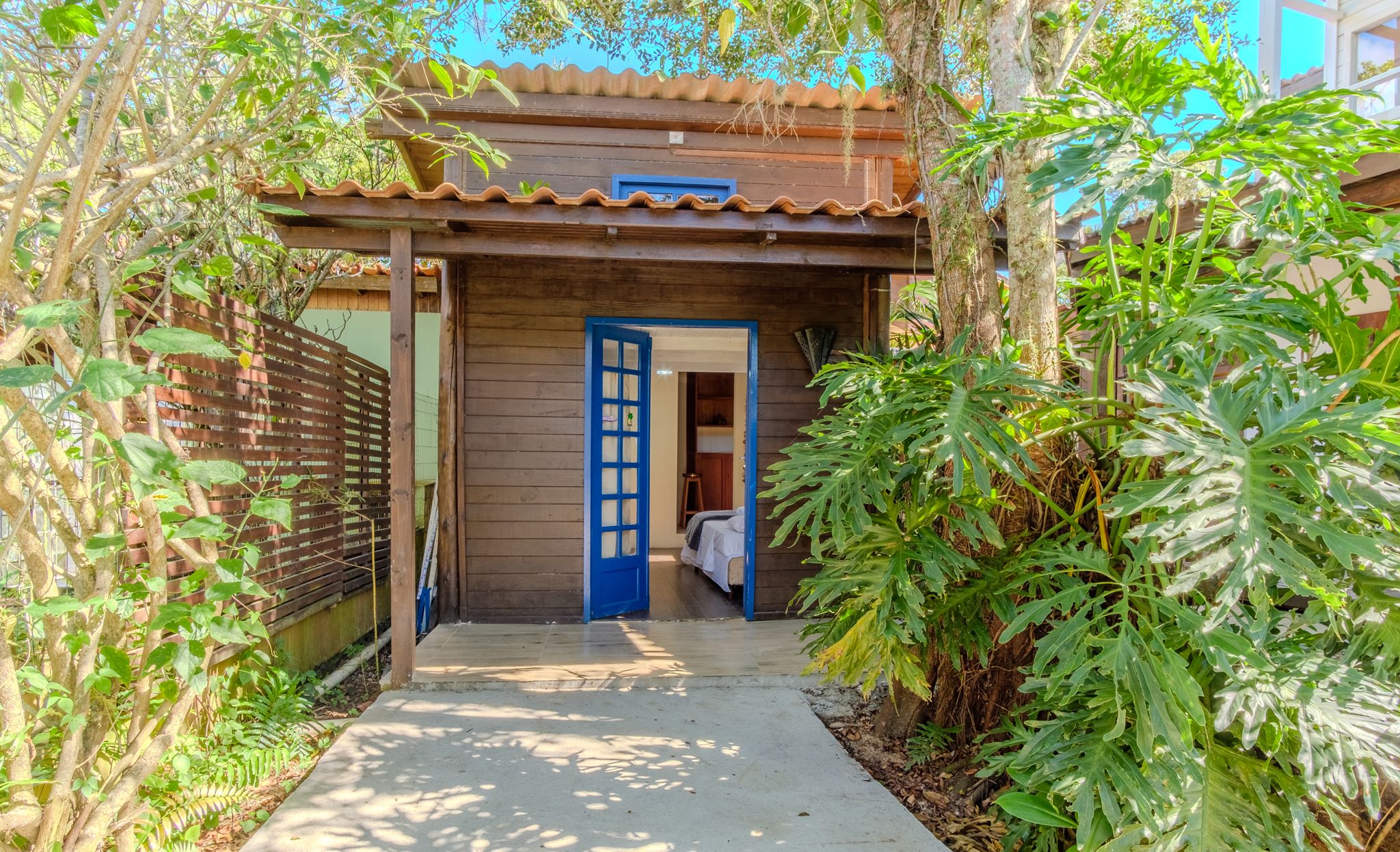 A wooden house with a blue door, a small porch, and a garden with various plants.