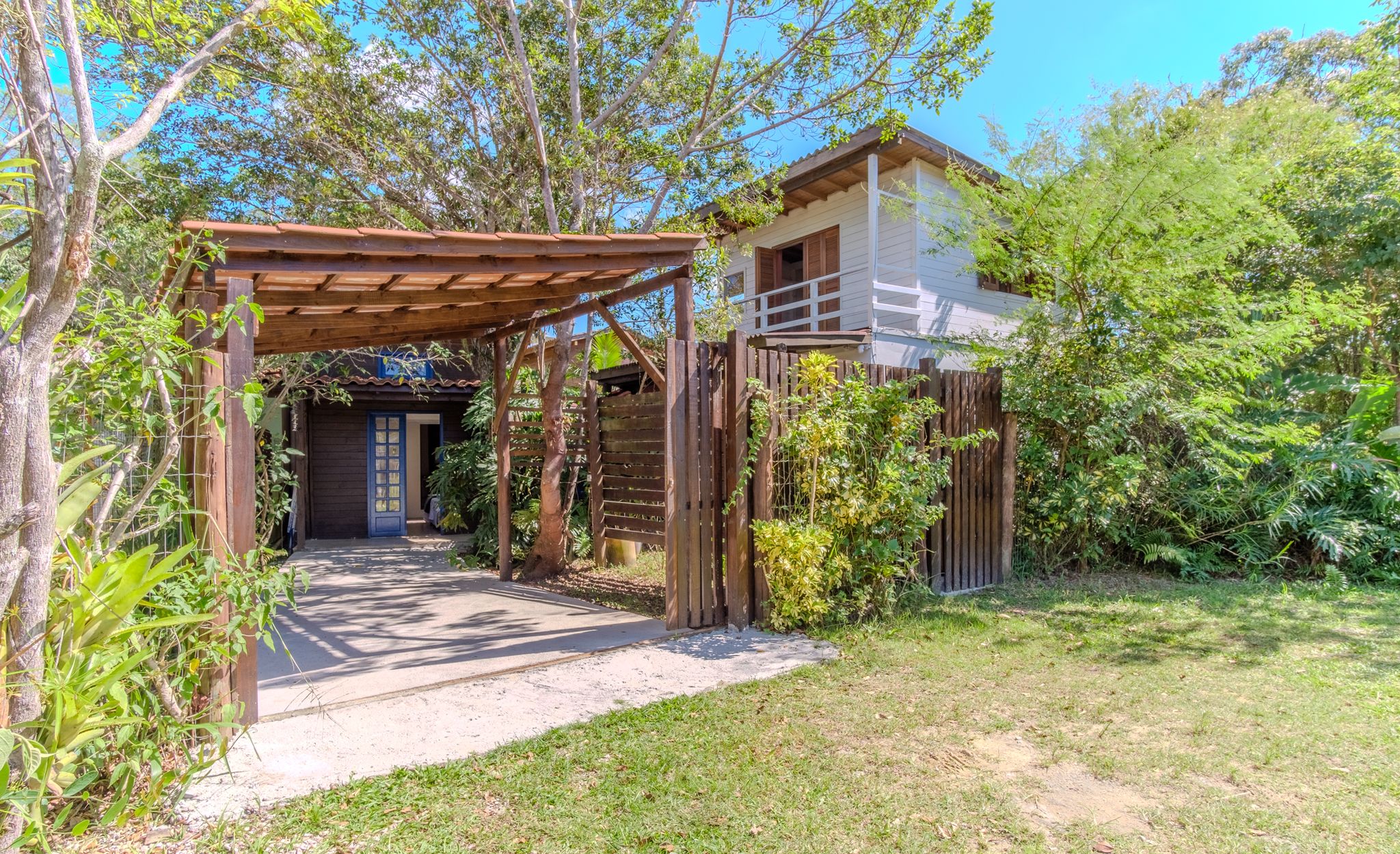 Una pérgola de madera que conduce a un edificio blanco con una puerta oscura.