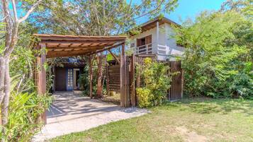 Una pérgola de madera que conduce a un edificio blanco con una puerta oscura.