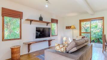 A living room with a television, wooden shelves, a bench, and a sofa with cushions.