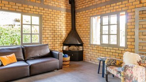 A cozy living room with a brick wall, a fireplace, a brown leather sofa, a floral armchair, and a small round table.