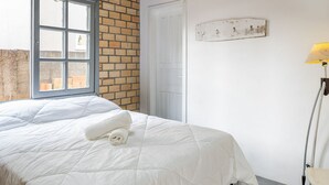 A bedroom with a large bed, a window, a door, and a lamp.