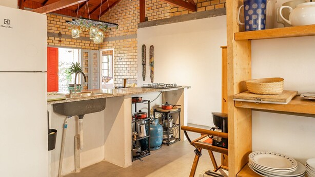 A kitchen with a brick wall, wooden beams, a gas stove, and various kitchen utensils.