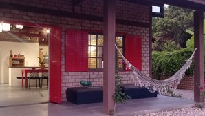 A brick building with red shutters, a hammock, and a dining area visible through an open door.