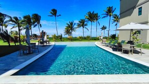 A swimming pool with lounge chairs and umbrellas, surrounded by palm trees and a clear sky.