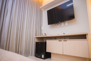 Una habitación con una televisión de pantalla plana montada en la pared, un mueble de madera debajo y un refrigerador negro a la izquierda.