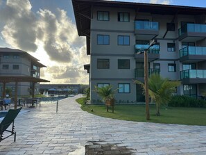 Un edificio moderno con varios balcones y un área de piscina con sillas de descanso y sombrillas.