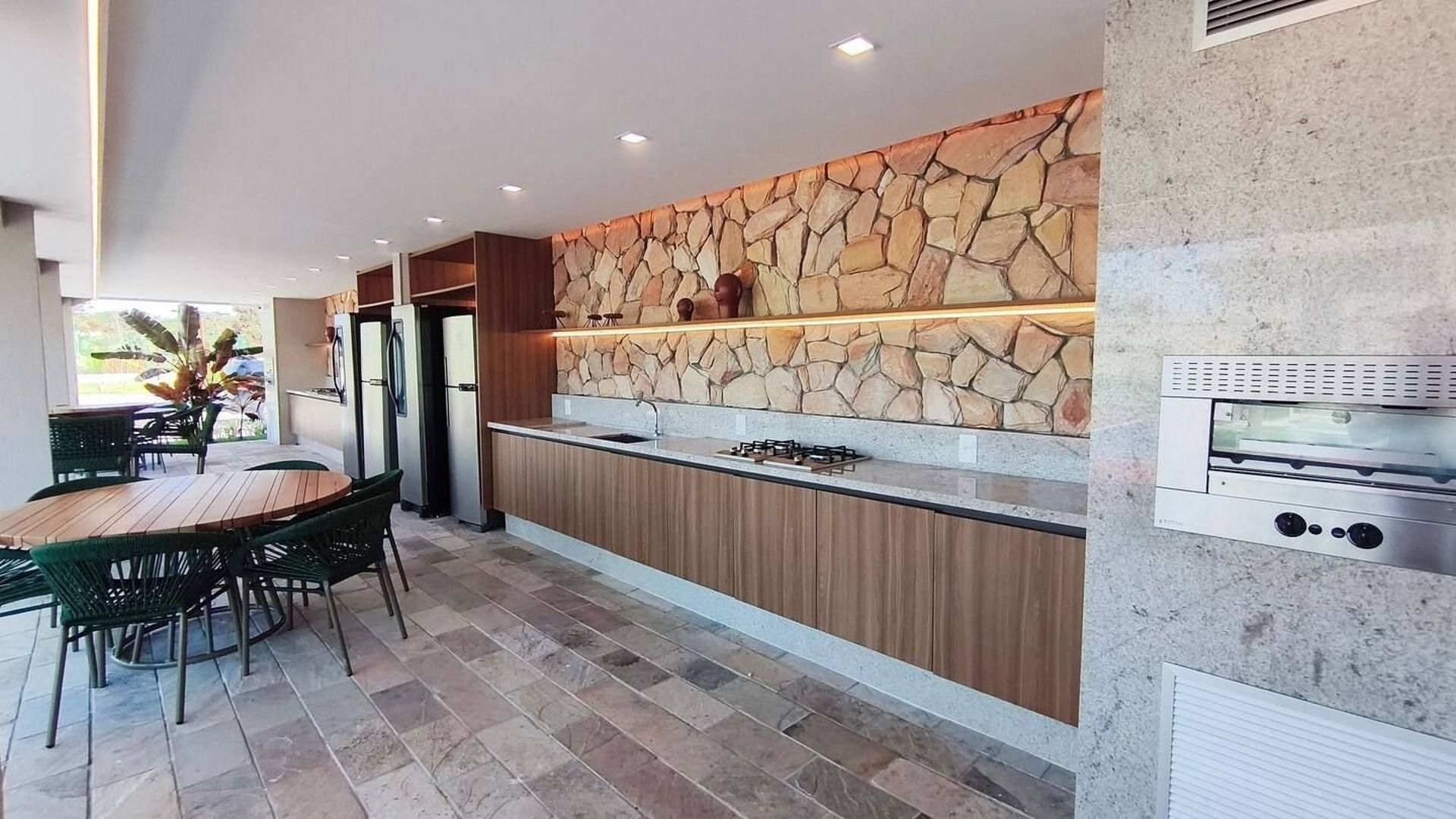 Cozinha moderna com painel de pedra, eletrodomésticos embutidos e área de jantar com assentos externos.