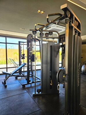 Un gimnasio con diversas máquinas de ejercicio, una banca y vistas al exterior a través de amplias ventanas.