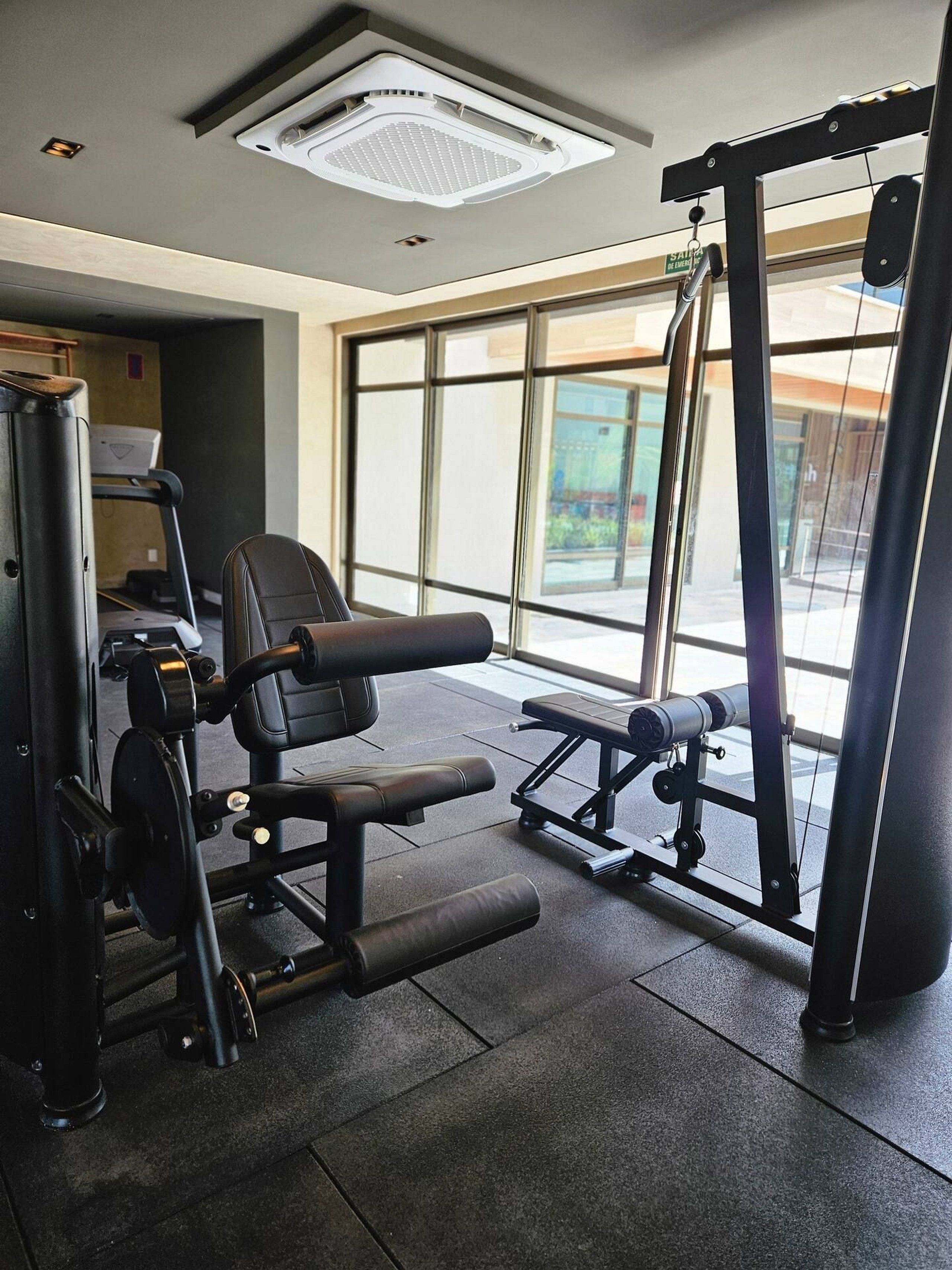 Un gimnasio con equipamiento de ejercicio, ventanas amplias y una lámpara en el techo.
