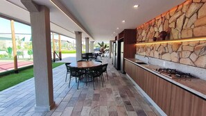 An outdoor dining area with a stone wall, a bar counter, and a view of a tennis court.