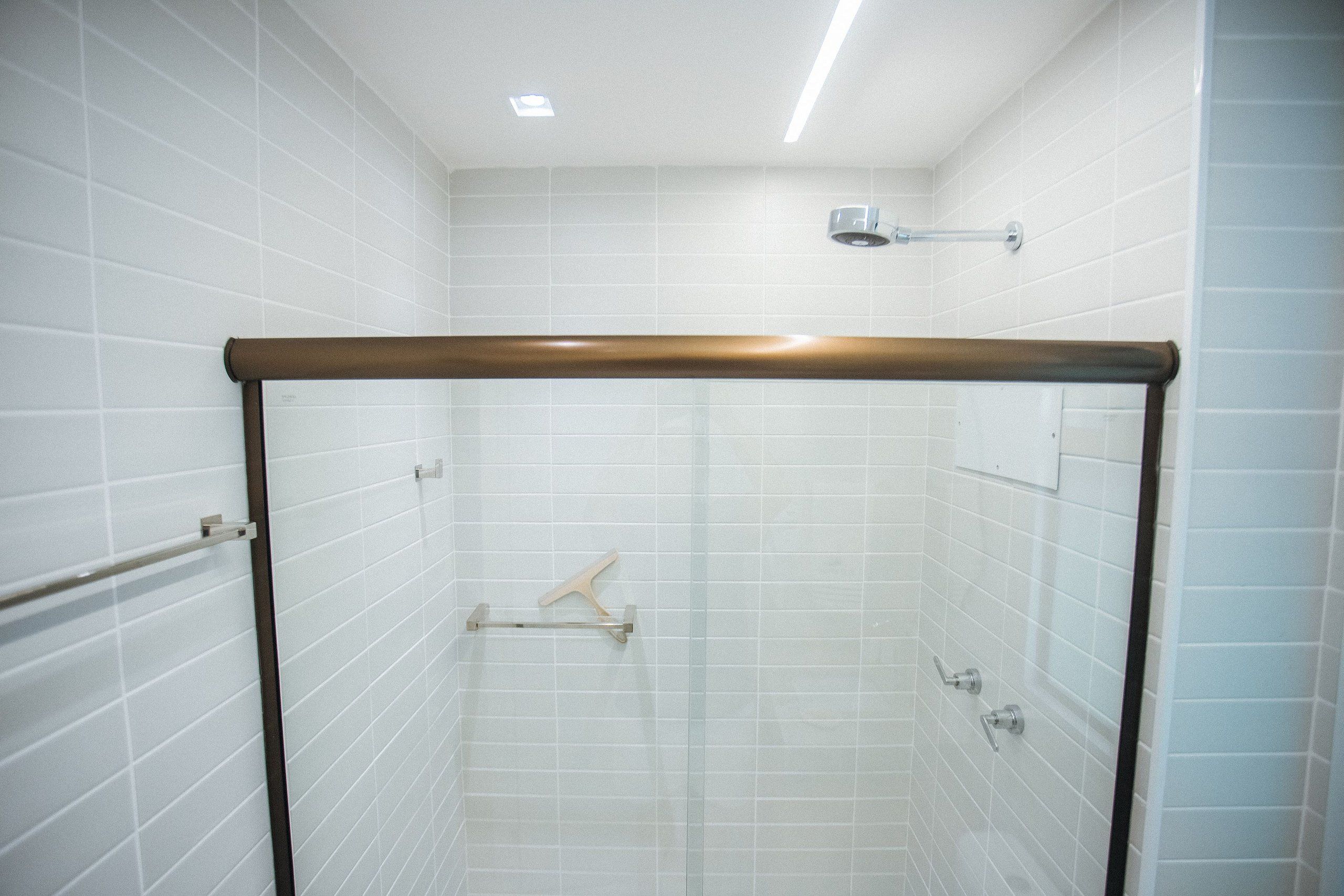 Una ducha moderna con paredes de azulejos blancos, estructura de madera y cabezal de ducha de mano.