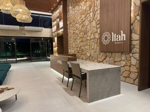 A modern interior with a stone wall, a reception desk, and a seating area. - Brisa em Muro Alto - Flat na Praia (Ipojuca)