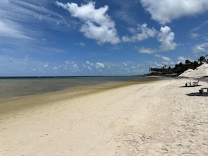 A beach with a clear sky, calm sea, and a few umbrellas on the right.