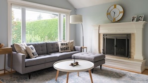 A living room with a grey sofa, a round coffee table, a fireplace, and a large window. - Private Garden Home in Madison Valley (Seattle)