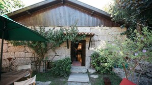 A rustic stone building with a wooden roof, a stone pathway leading to a wooden door, and a green umbrella.