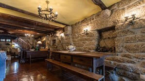 A rustic kitchen with stone walls, wooden beams, and a bench.