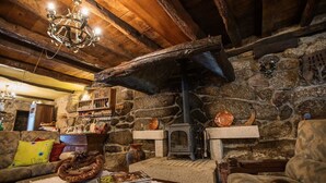 A rustic interior with exposed wooden beams, a stone wall, a fireplace, and a chandelier.