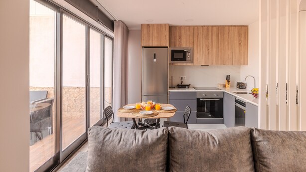 Una cocina moderna con armarios de madera, un refrigerador, microondas y una zona de comedor con una mesa preparada para dos.