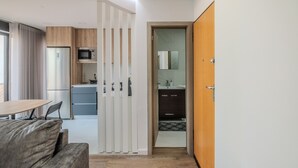 Una cocina moderna con refrigerador, microondas y gabinetes de madera. Hay un comedor con mesa y sillas, y un baño independiente con espejo y lavamanos.