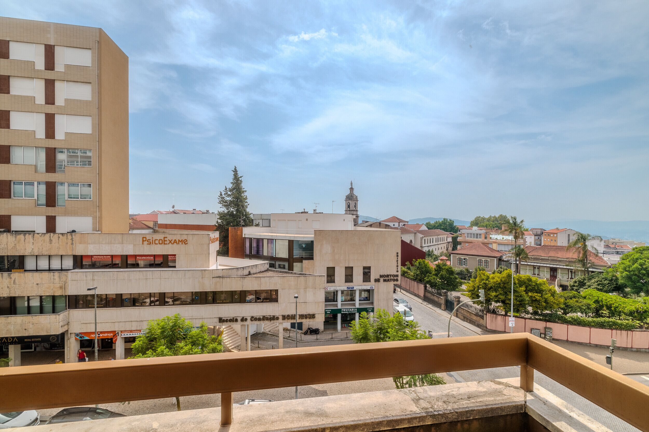Une vue depuis un balcon donnant sur un paysage urbain, avec des bâtiments, dont une école et une pharmacie.