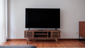 A modern living room with a large flat-screen TV mounted on a wooden TV stand, hardwood flooring, and a neutral-colored rug.