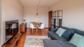 A modern living room with a sofa, a TV, a dining table with chairs, and a bookshelf.