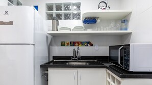 A kitchen with white cabinets, a black countertop, a stainless steel sink, a microwave, and a refrigerator. - Fully Equipped Apartments in the Best Location Just Steps From the sea in Guarapari - STP (Guarapari)