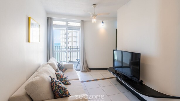 A modern living room with a sofa, TV, and a balcony view. - Fully Equipped Apartments in the Best Location Just Steps From the sea in Guarapari - STP (Guarapari)