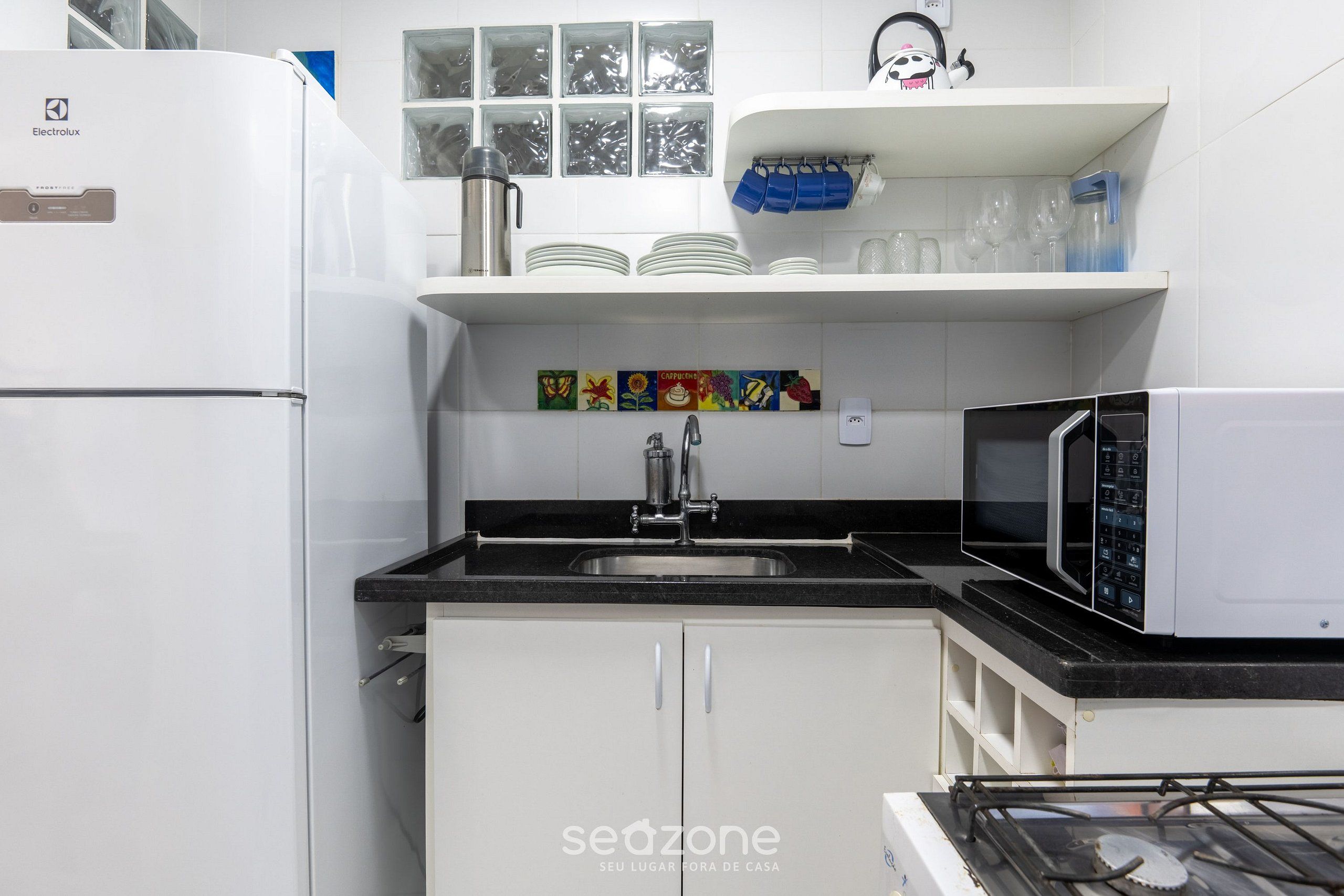 A kitchen with white cabinets, a black countertop, a stainless steel sink, a microwave, and a refrigerator.