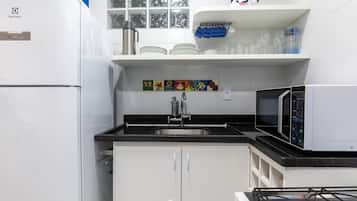 A kitchen with white cabinets, a black countertop, a stainless steel sink, a microwave, and a refrigerator.